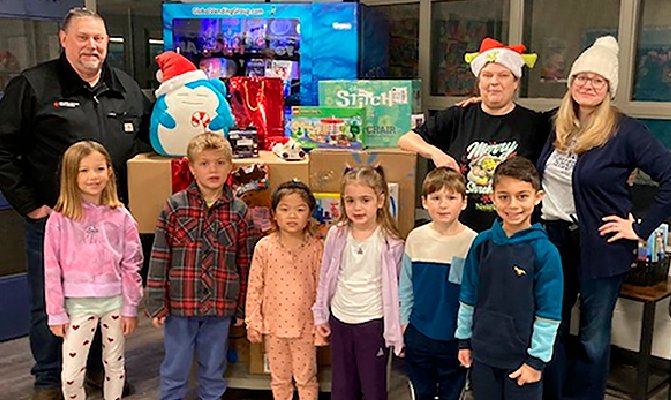 Six children and three adults are standing around the present.
