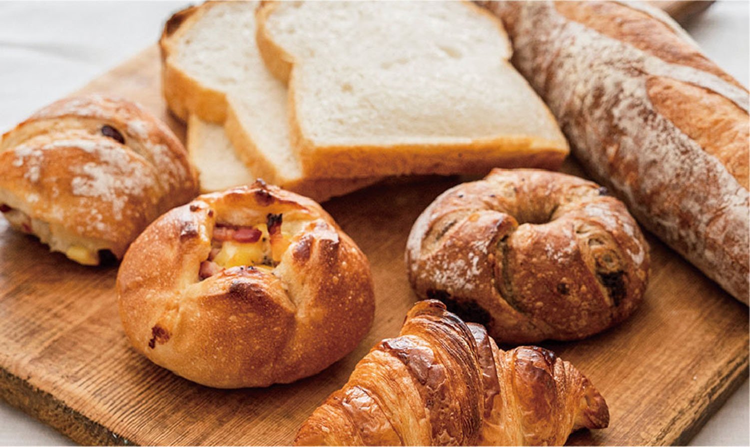 木製のトレーの上に、フランスパン1本、スライスされた食パン3枚、ベーグルのような丸形のパン3個、クロワッサン1個が並べられています。
