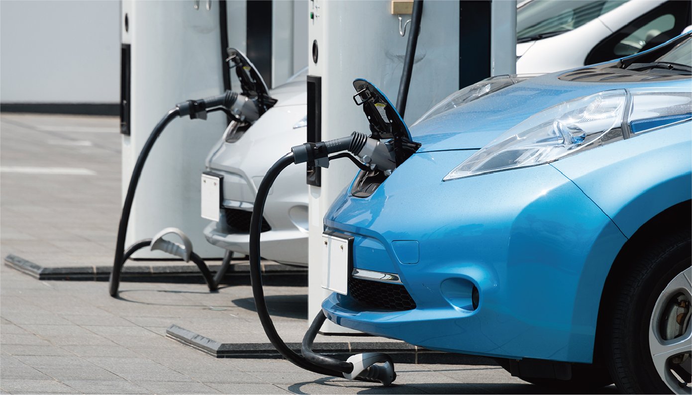 青とシルバーの２台の電気自動車がフロントのプラグに充電器のコネクタを繋いで充電しています。