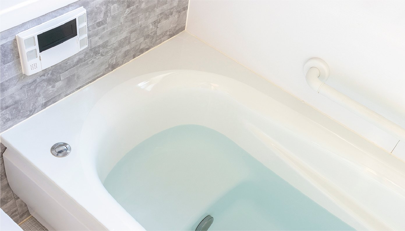 背面がマーブル調で側面が白色の浴室に白色の浴槽があり、水が張られています。