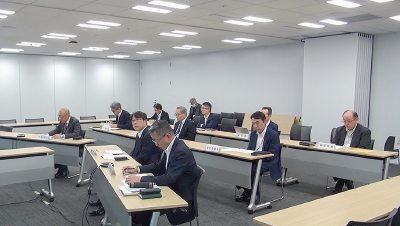 This is a photograph showing multiple executives and employees seated at a table with their laptops open, participating in a joint company-wide BCP drill in a conference room.
