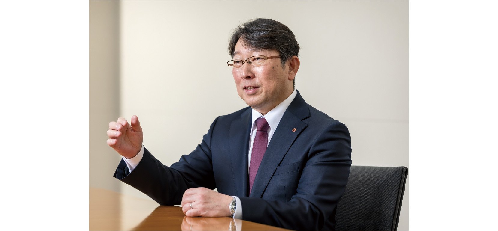 This is a photograph of Representative Director Koji Sawamura, shown speaking with a serious expression while making gestures and slightly raising his right hand.
