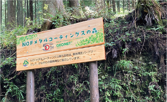 The sign is made of two wooden posts with a wooden board attached, and it says “NOF Metal Coatings Forest”.