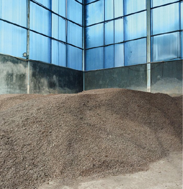 In a warehouse surrounded by translucent walls that let in light, there is a pile of crushed coconut shells piled up like a mountain.
