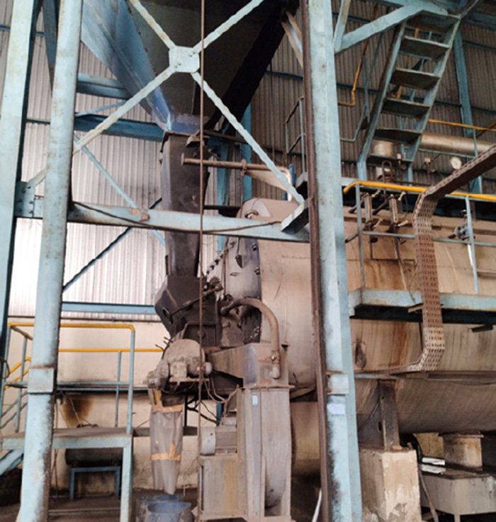 There is a steel frame in a large, warehouse-like space with a high ceiling, and a large incinerator boiler is installed.