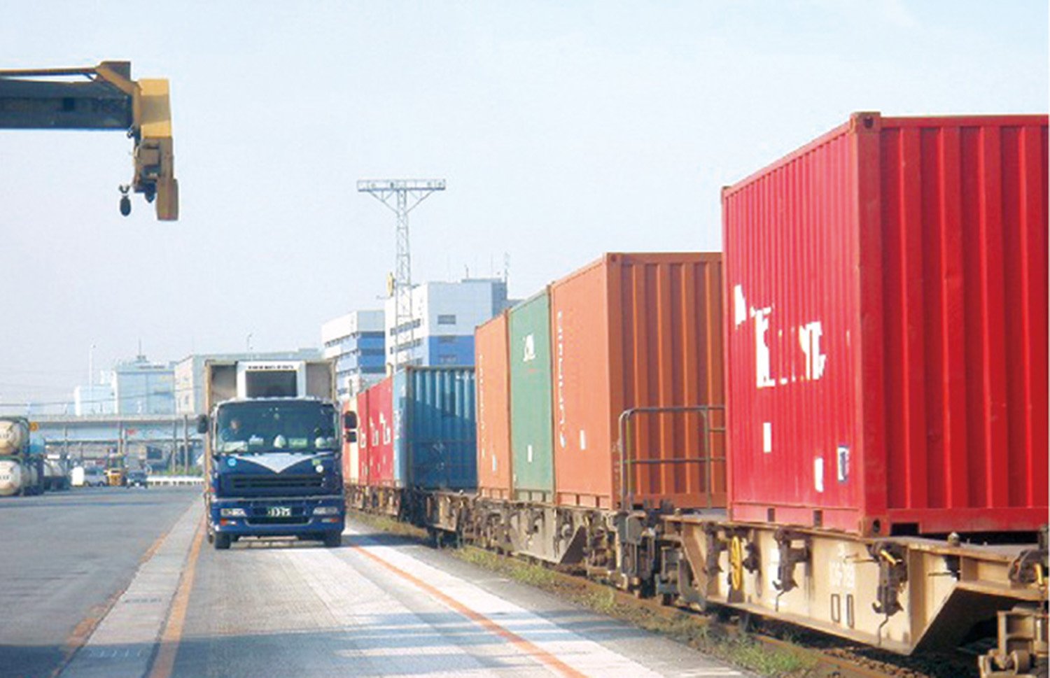 A straight road stretches from the front to the back, and to the left of the road is a square, while to the right there are countless containers lined up on platforms.