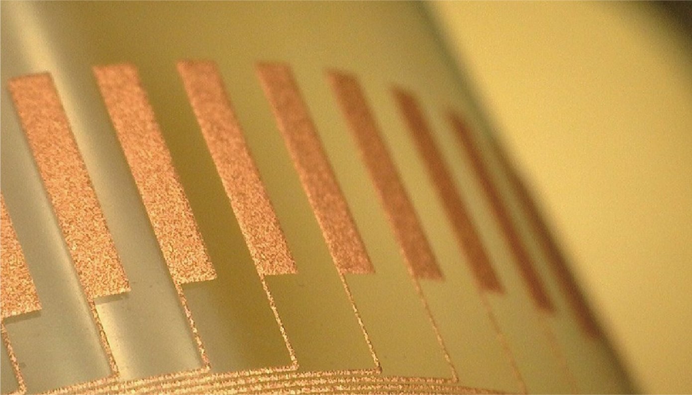 On a translucent resin film, thick vertical bars are printed in parallel at equal intervals using copper ink. They are connected in the lower direction by thin lines.