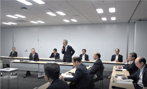 長テーブルがコの字型に並べられた会議室に本社部門長が着席して、机上訓練を行っていて、担当役員が訓示をしています。