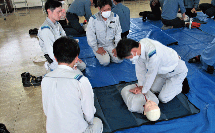 一人が訓練模型の人形を使って心臓マッサージの訓練をしています。その回りに3人が訓練を見守っています。