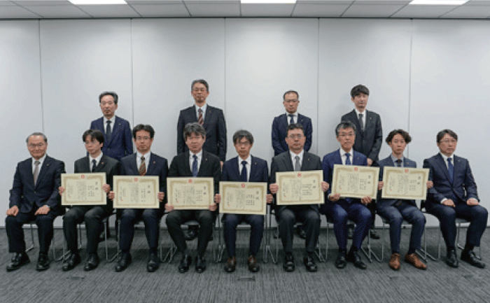 This is a group photo of the two rows of people in front and back. The seven people who received awards are seated in the front row with their certificates, and the chairman and president are seated on either side of them. There are four people standing behind them at equal intervals.
