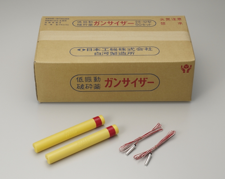 ガムテープで封をした段ボールが1箱おいてありその下側に黄色い筒に赤いテープをした製品2本と導火線2組が並べられています。